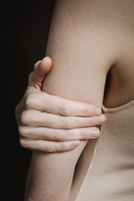 Crop anonymous person with bare shoulder and hand holding arm against black background